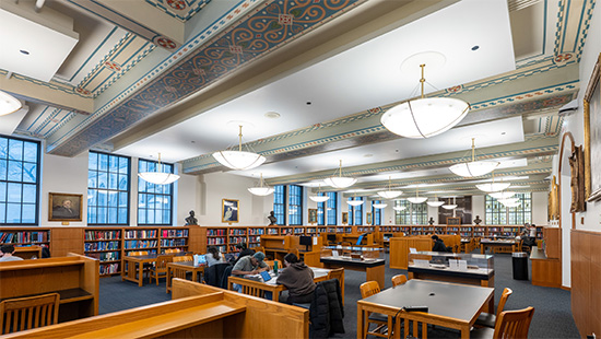 A wide view of the Galter Library reading room, filled with tables and chairs. The ceiling is accented with blue and orange tile-like patterns.